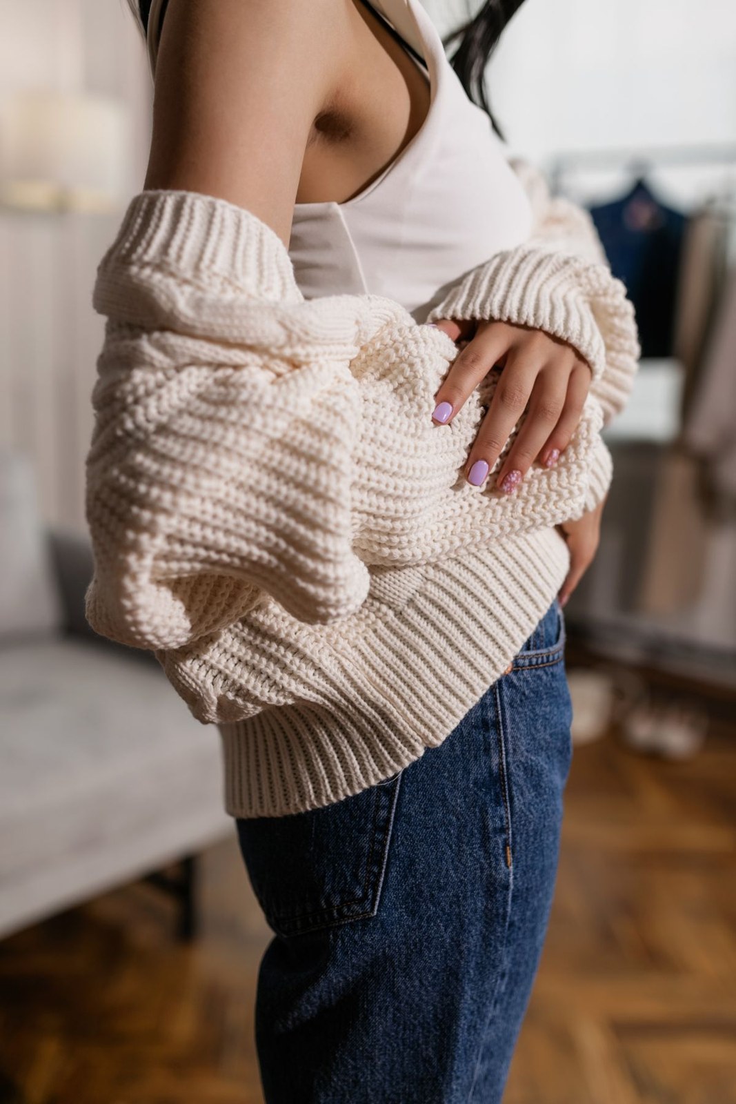 Cream chunky cardigan worn loosely over a light tank top and blue jeans; only the upper body and jean waist are visible.