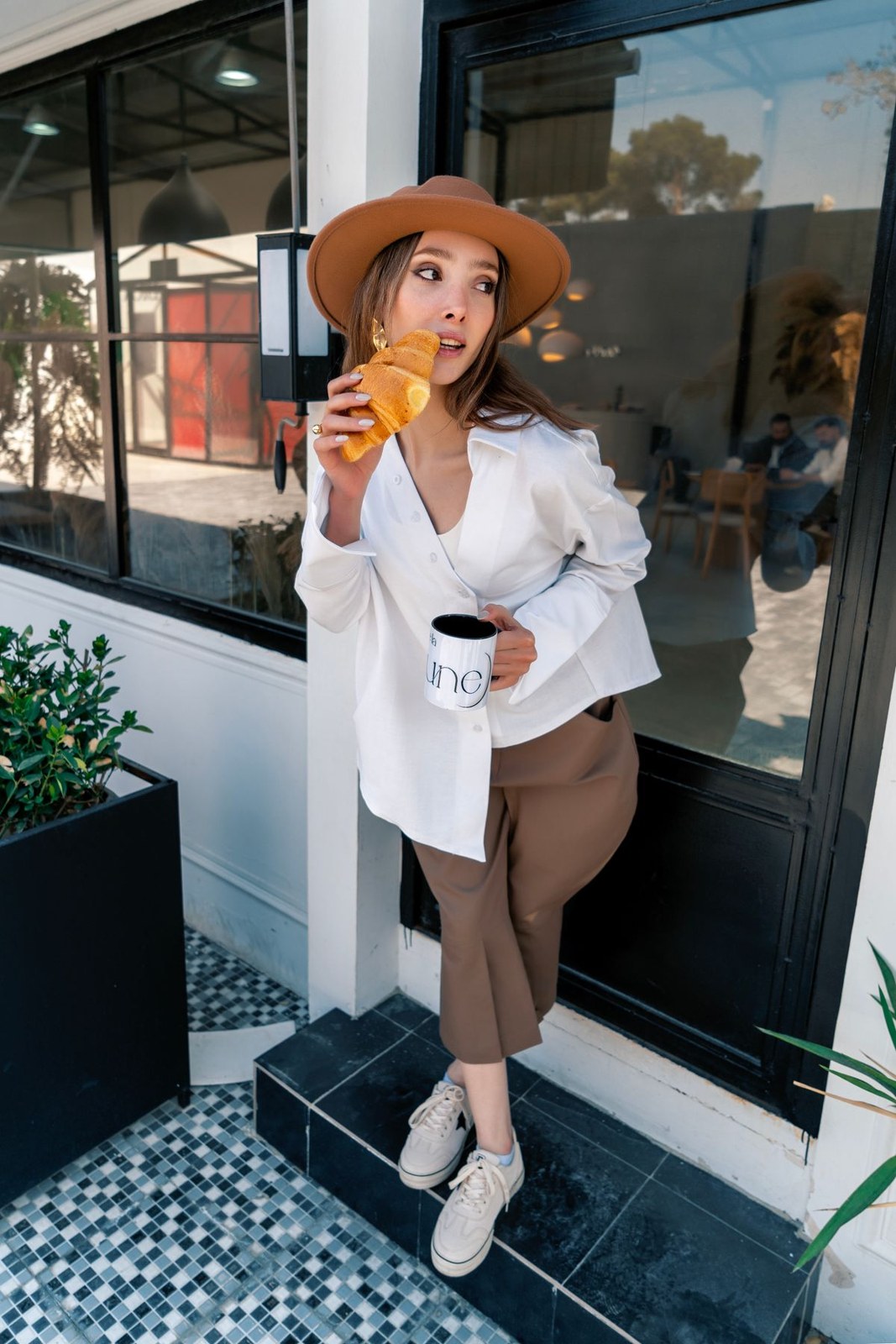 White blouse with brown belted cropped trousers, white ankle boots and a tan brimmed hat.