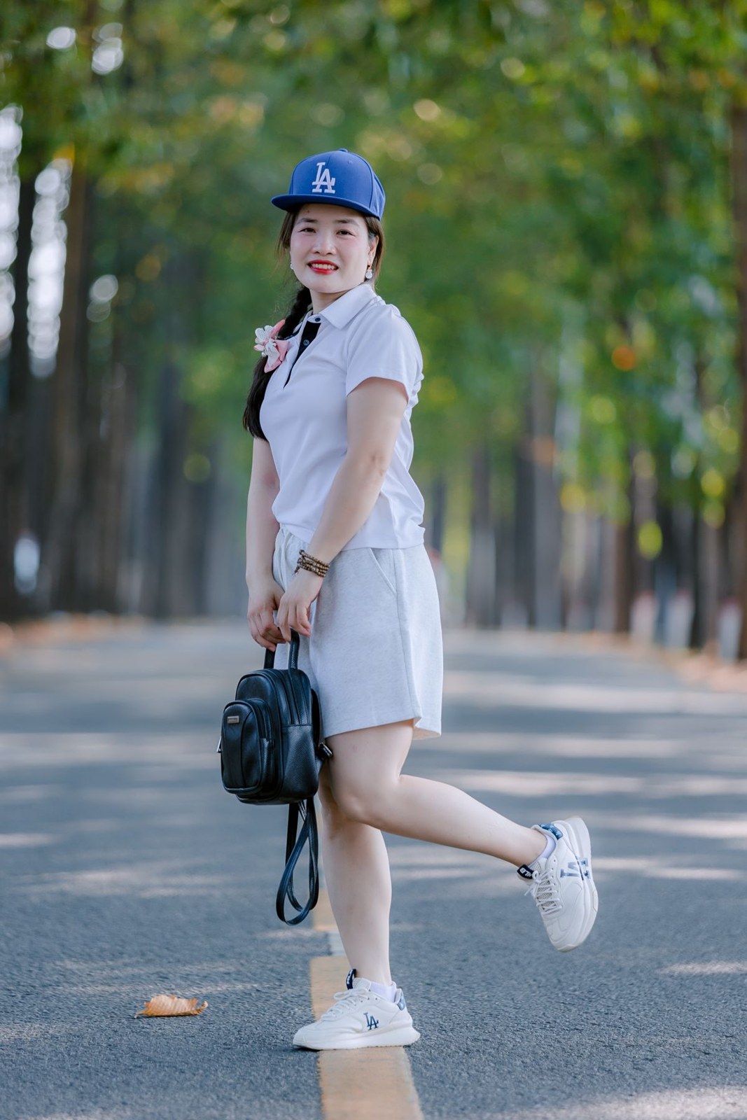 Short white collared dress, blue baseball cap, white socks and trainers, and a dark backpack.