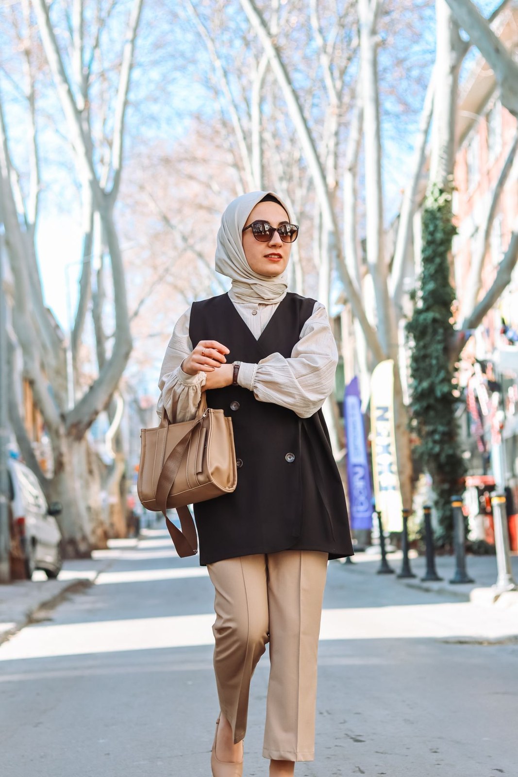 Cream headscarf, white blouse, long black sleeveless vest, beige cropped trousers, tan handbag and sunglasses.