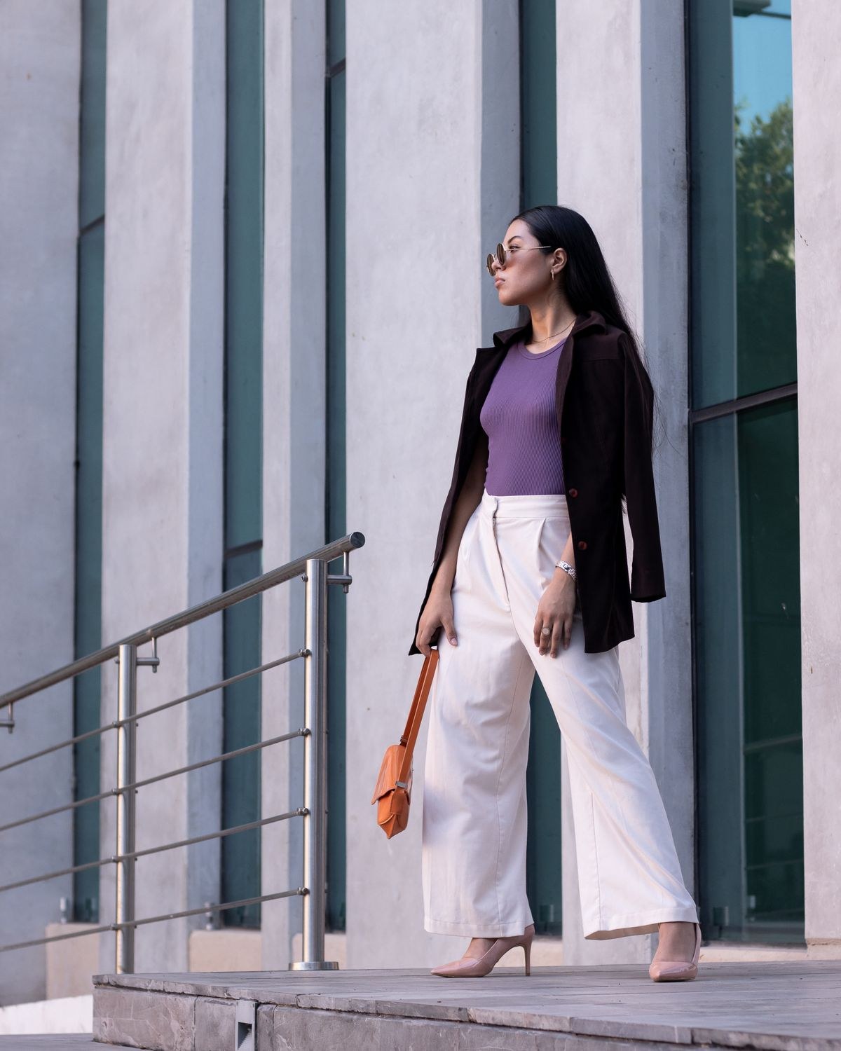 Black blazer over a purple top with cream wide-leg trousers, pale heels and an orange handbag.