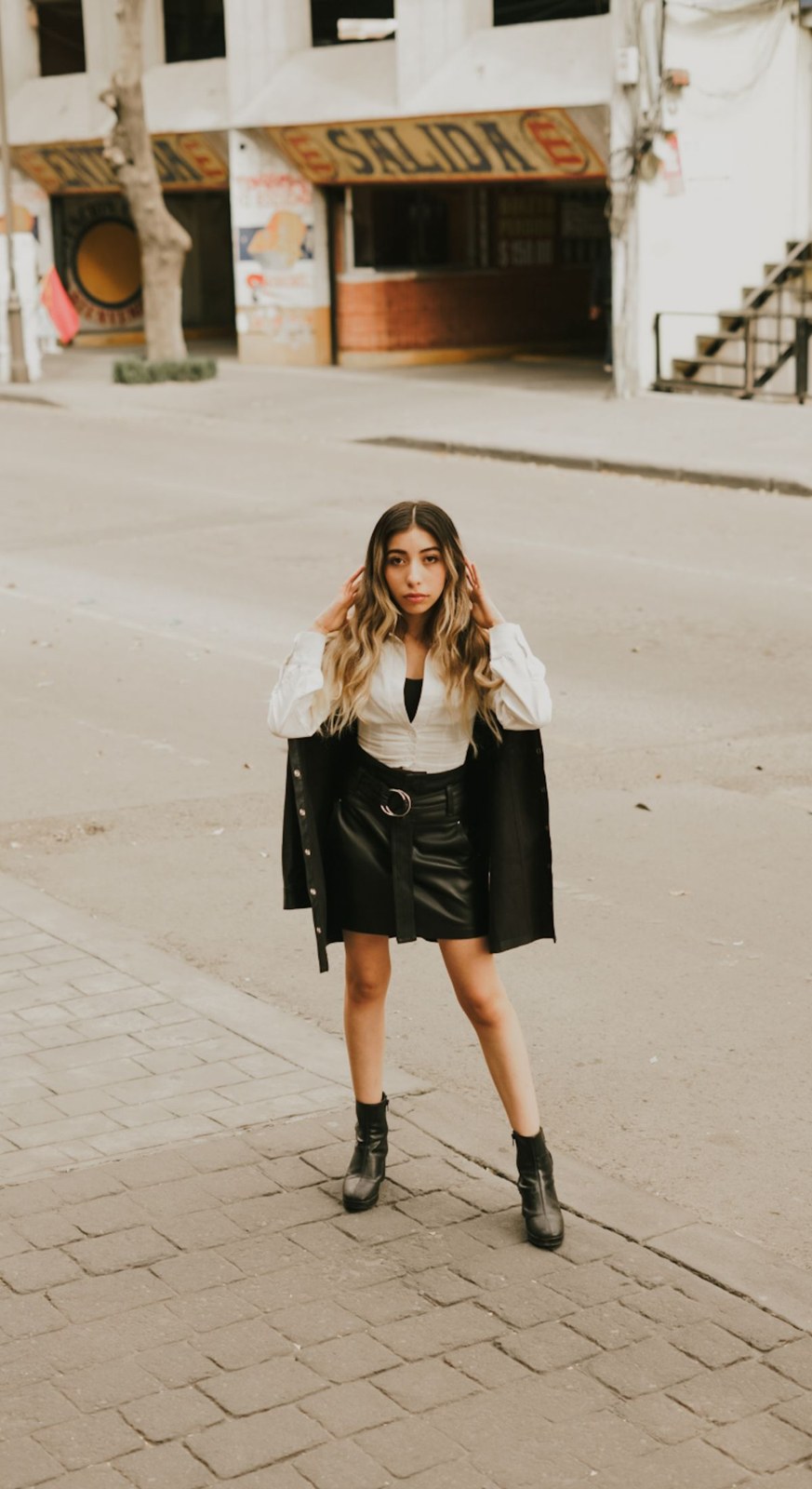 Black jacket draped over the shoulders, white shirt, black miniskirt and black ankle boots.