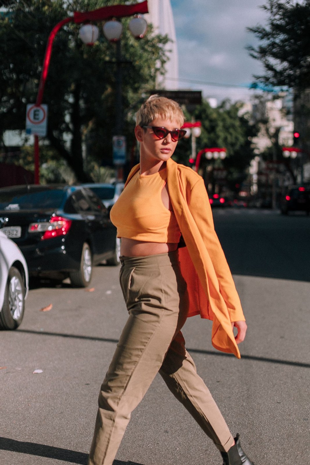 Mustard sleeveless top, checked brown trousers and orange outer layer, with sunglasses.