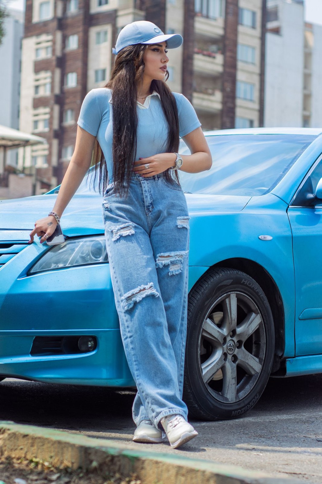 Pale-blue cropped T-shirt, ripped loose jeans, pale cap and white trainers.