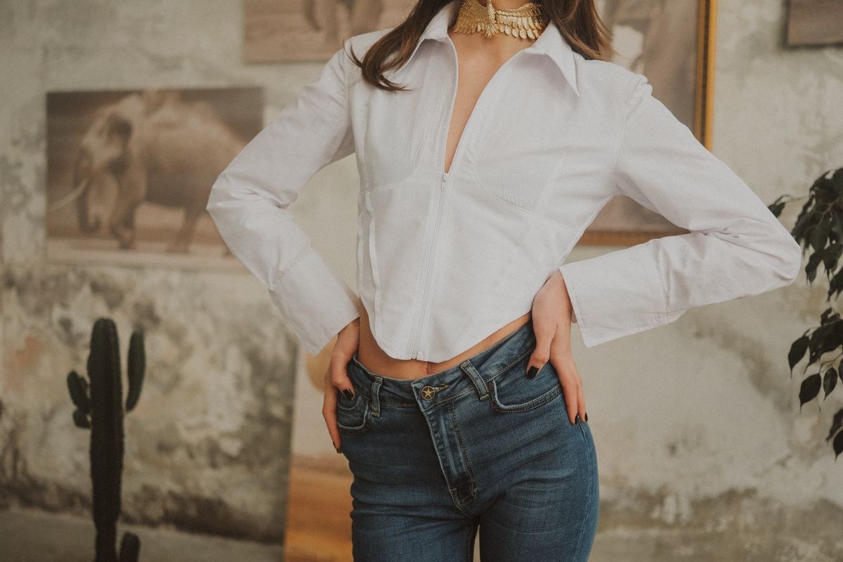 White collared blouse with a loose neckline tucked into blue jeans; waist detail.