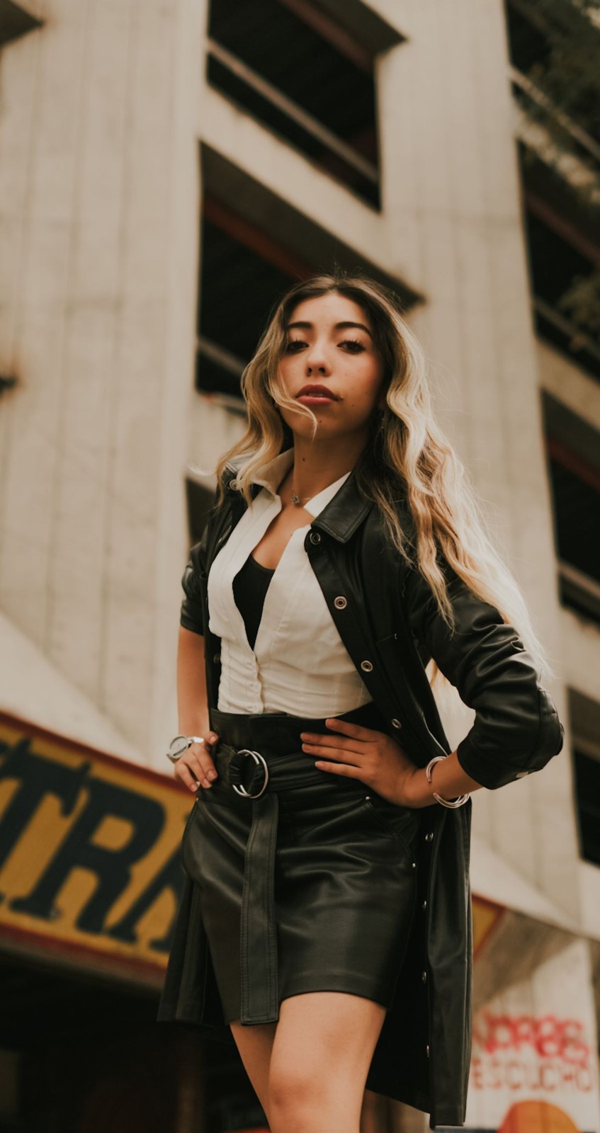Dark jacket, white V-neck top, black short skirt and a dark belt; thigh-level crop.
