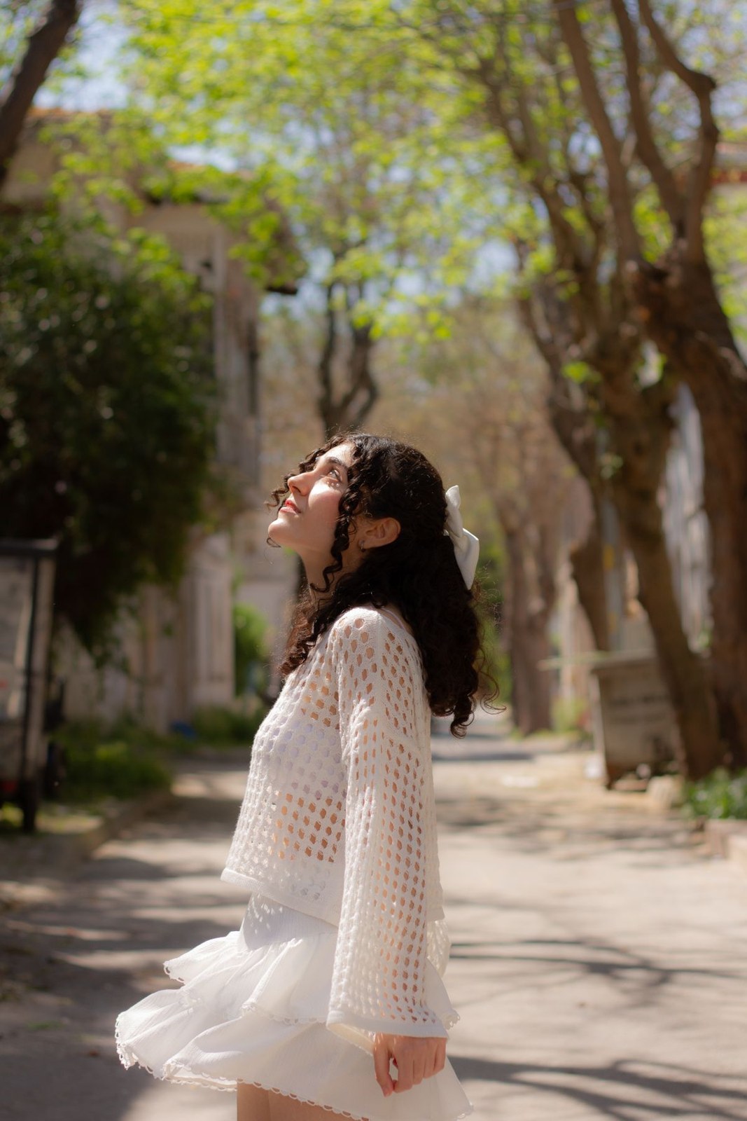 Loose white open-knit sweater and short white skirt in a leafy outdoor setting.