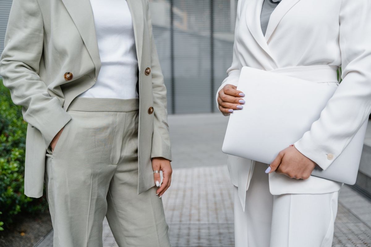 Cropped detail of two pale trouser suits: belted beige and white wrap blazer, with white document folders.