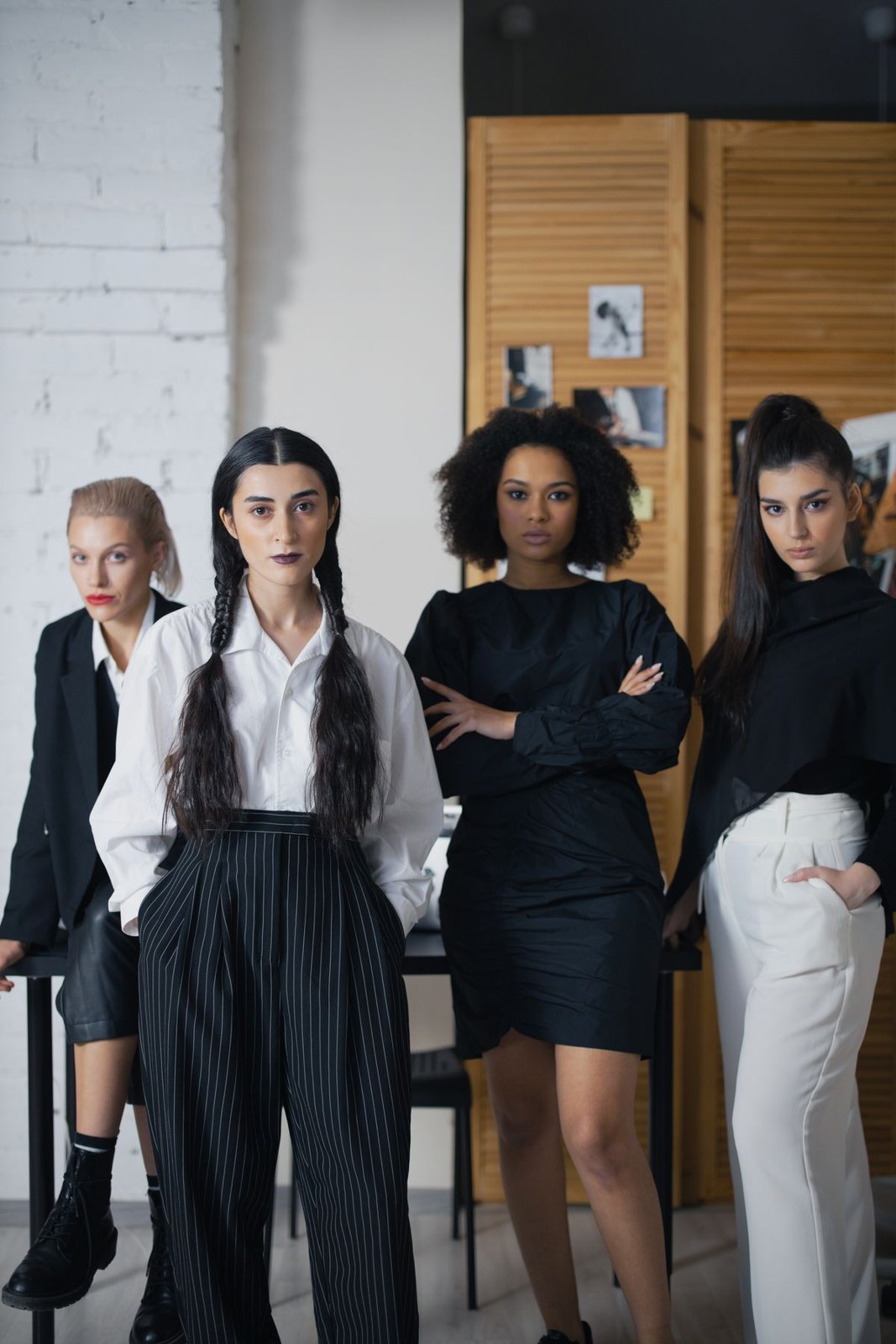 Four women in black-and-white outfits; front woman in a white collared shirt, black tie and long black pleated skirt.