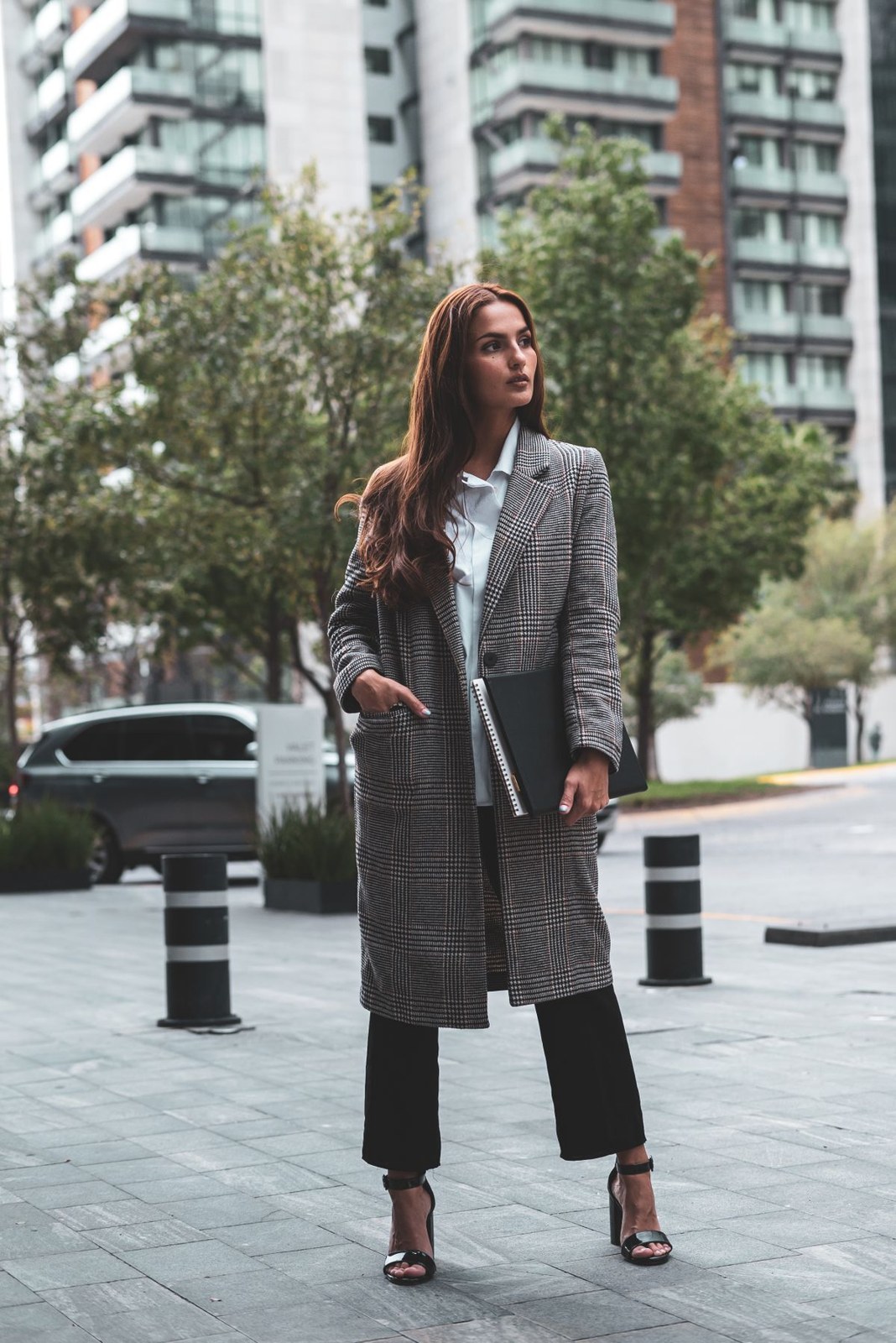 Long grey checked coat over a white shirt and black cropped trousers with strappy black heels.