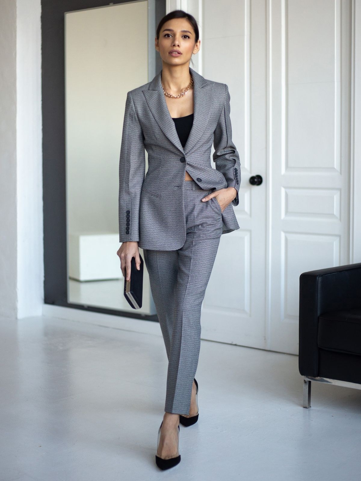 Grey single-breasted trouser suit with a black V-neck top, black pointed heels and a dark folio.