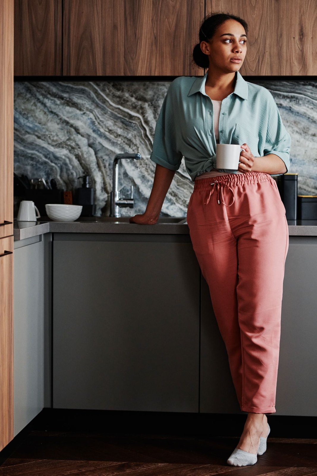 Pale-blue collared blouse, rust high-waisted trousers and white shoes while holding a cup.