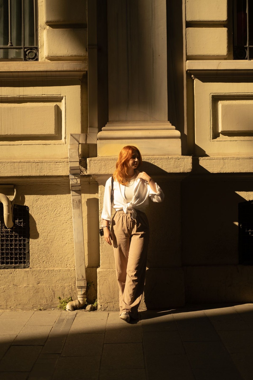 Loose white blouse tucked into tan high-waisted wide-leg trousers outdoors.