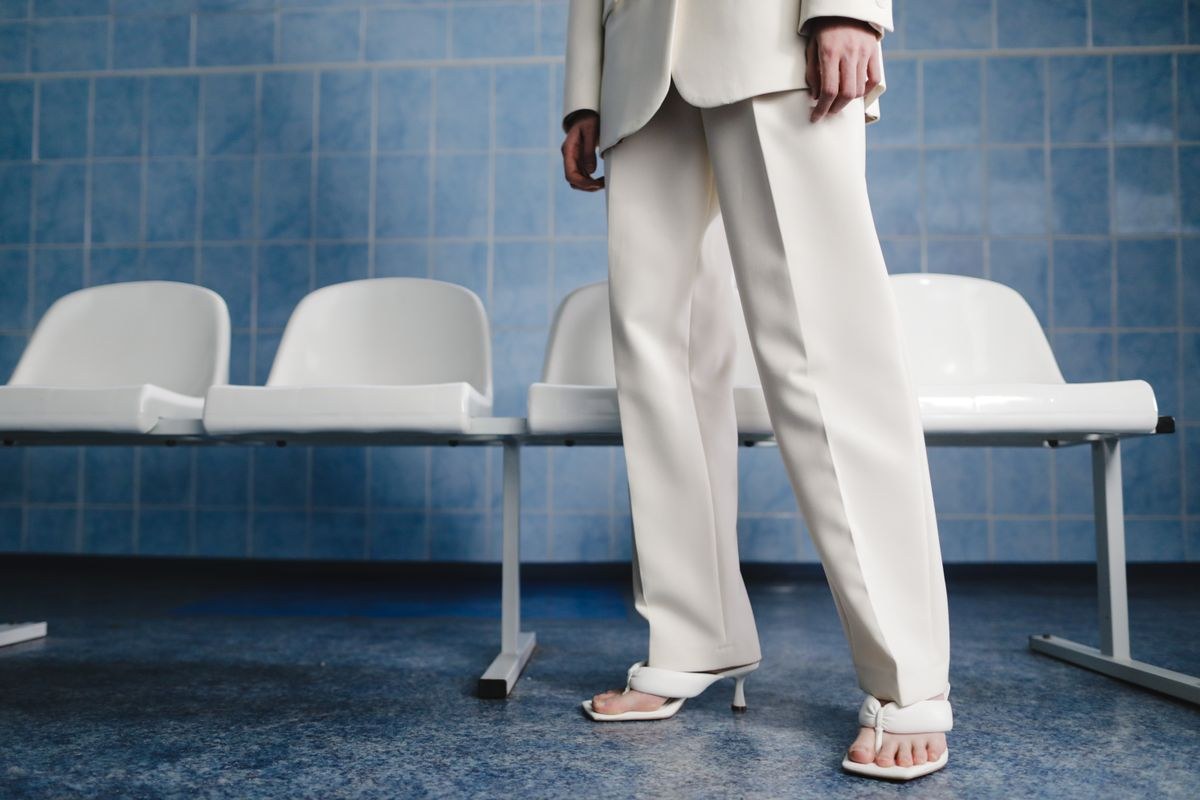 Pale neutral trouser suit and white open-toe heels; photograph focuses on the lower body.