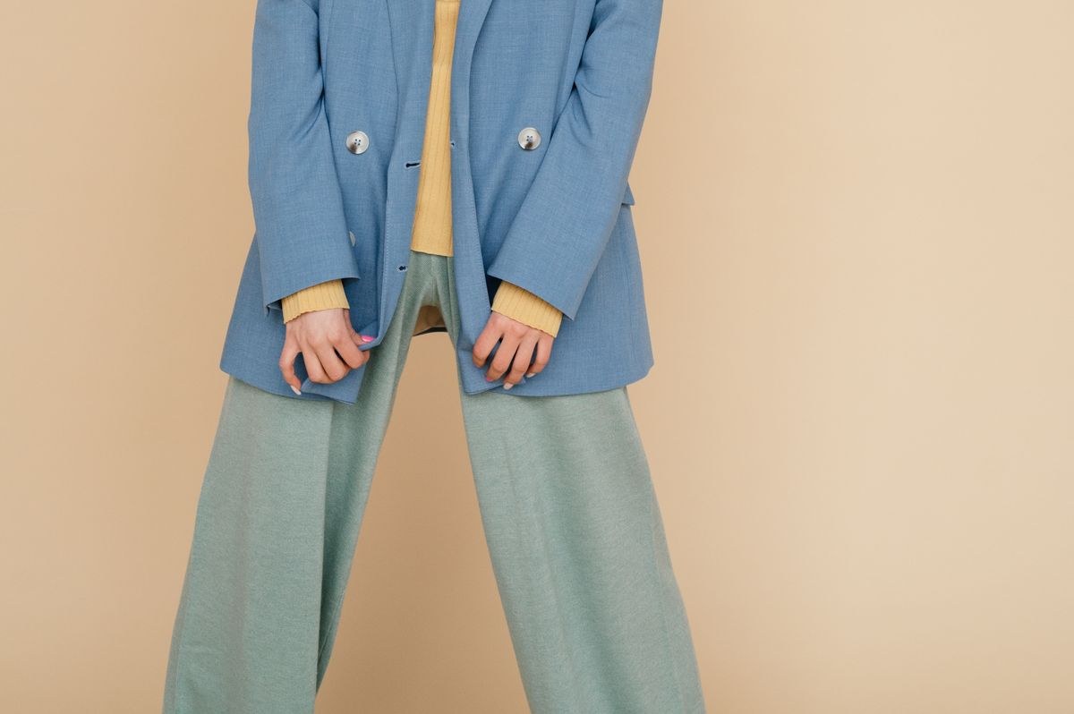 Blue double-breasted blazer with yellow cuff accents and pale wide-leg trousers; detail crop.