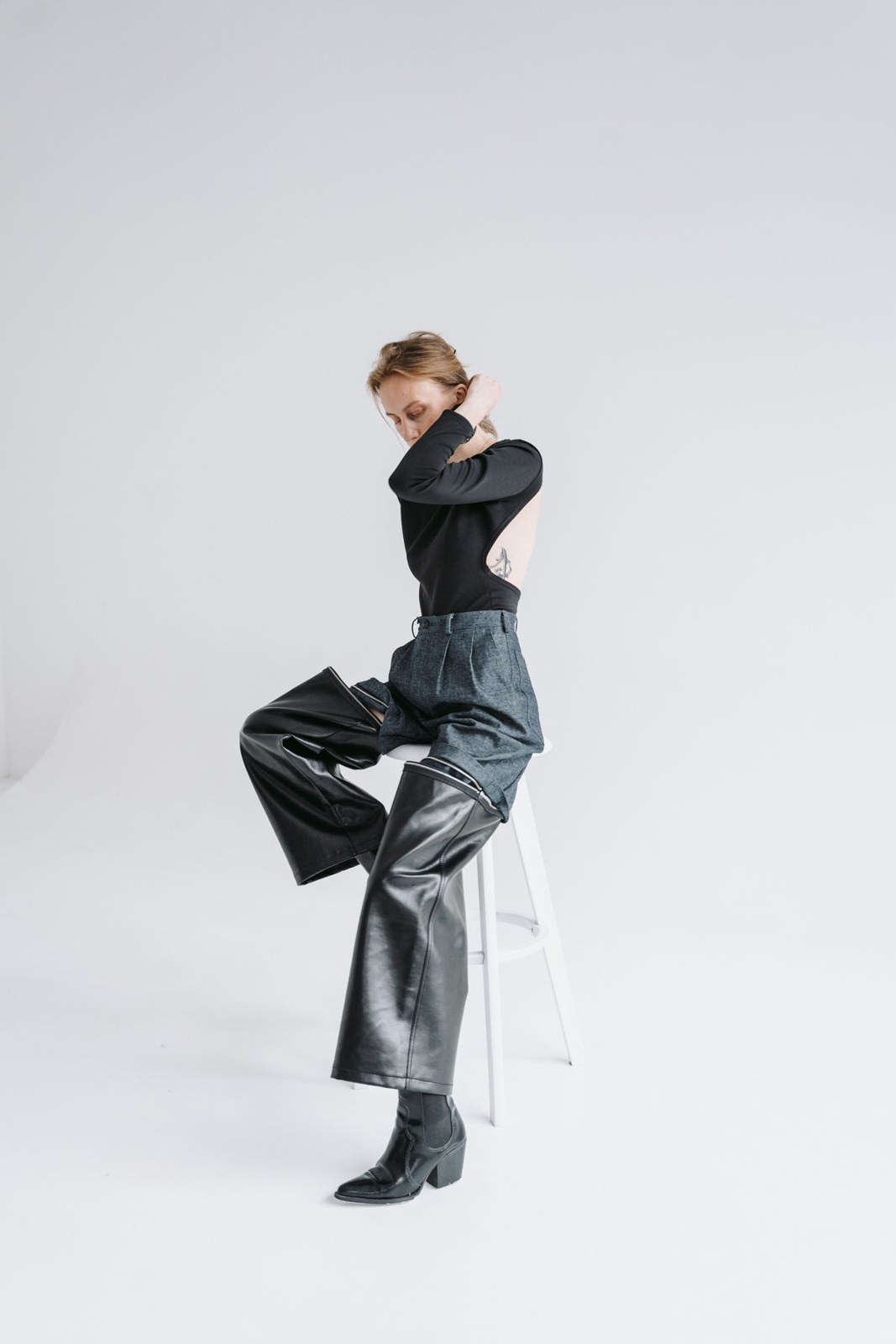 Black long-sleeve top, dark shiny wide-leg trousers and black ankle boots on a studio stool.