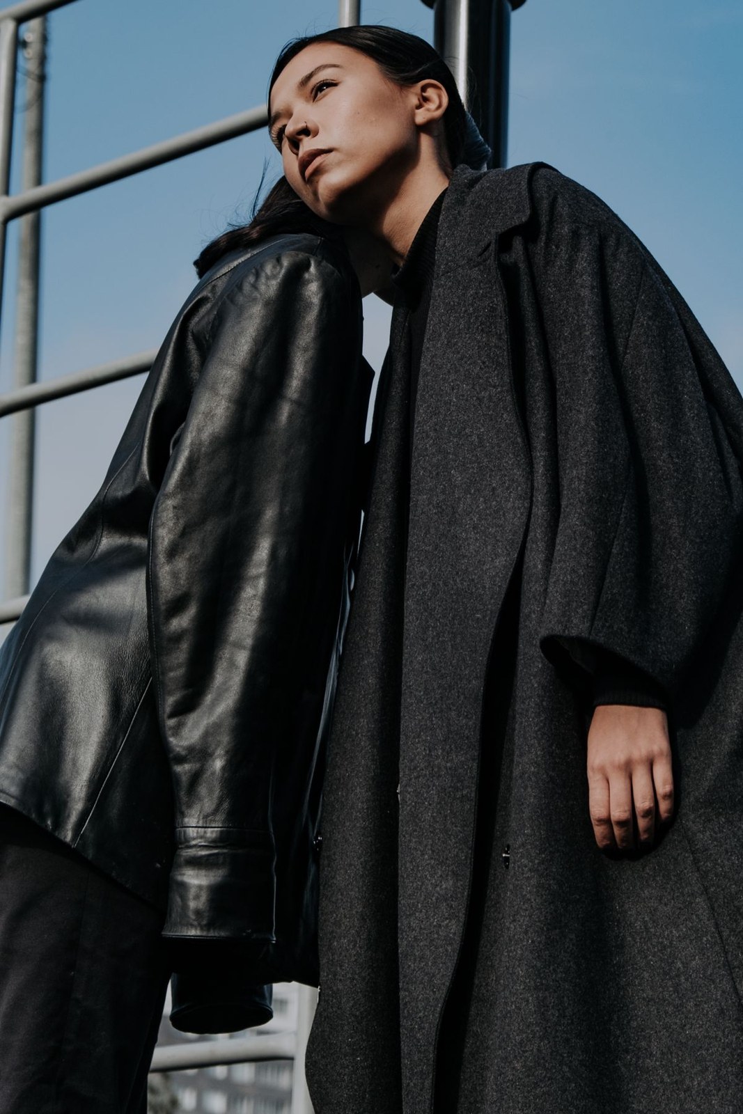 Long dark textured coat layered over a black high-neck top; low-angle upper-body portrait.