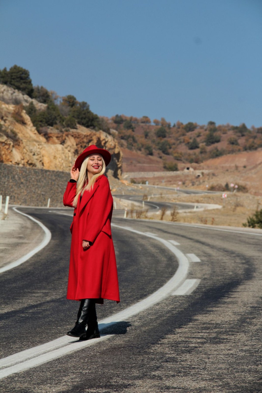 Bright red long coat with a matching red beret and dark boots on an open road.