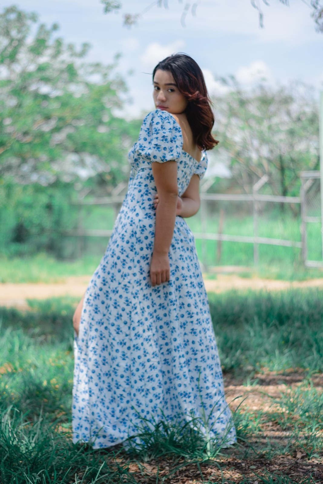 Long pale-blue floral dress with short puff sleeves, a defined waist and a loose full skirt; footwear is hidden by the hem.