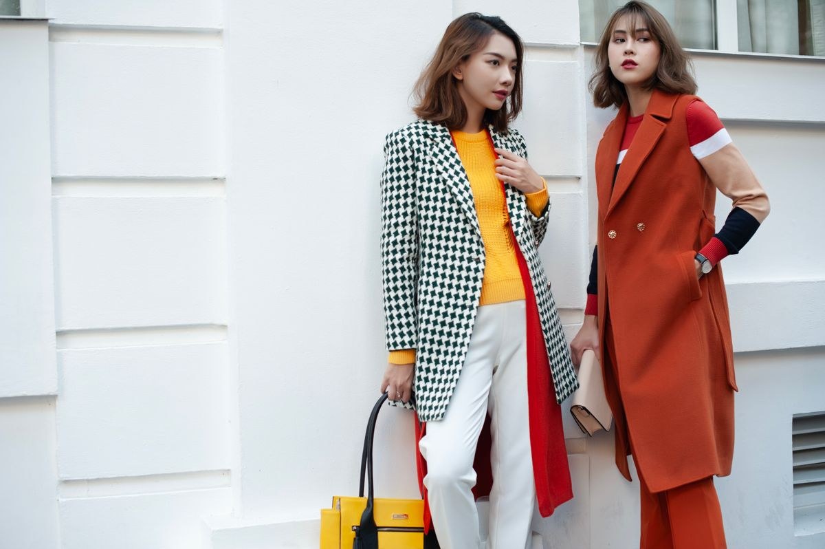 Checked coat, mustard top, white trousers and yellow bag beside a rust-orange long vest and matching trousers.