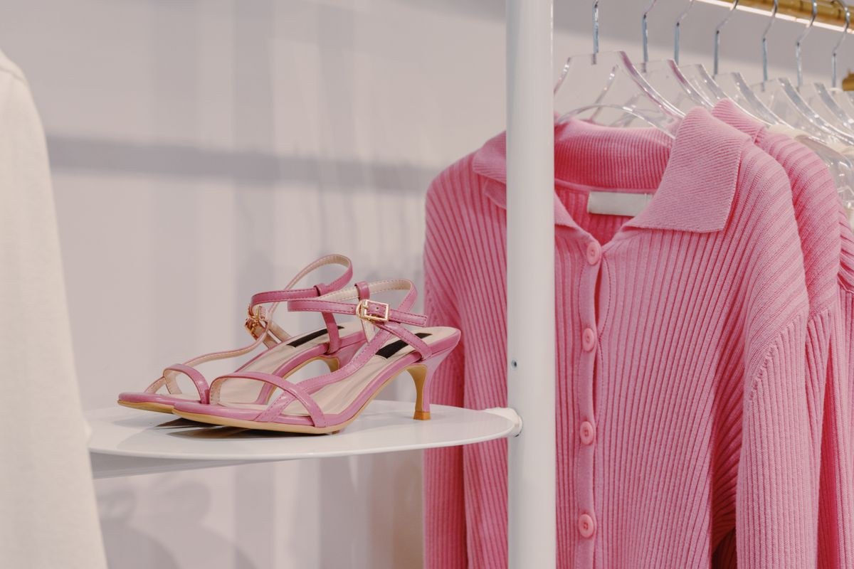 Pink ribbed knitwear on a hanger beside pink strappy sandals displayed on a stool.