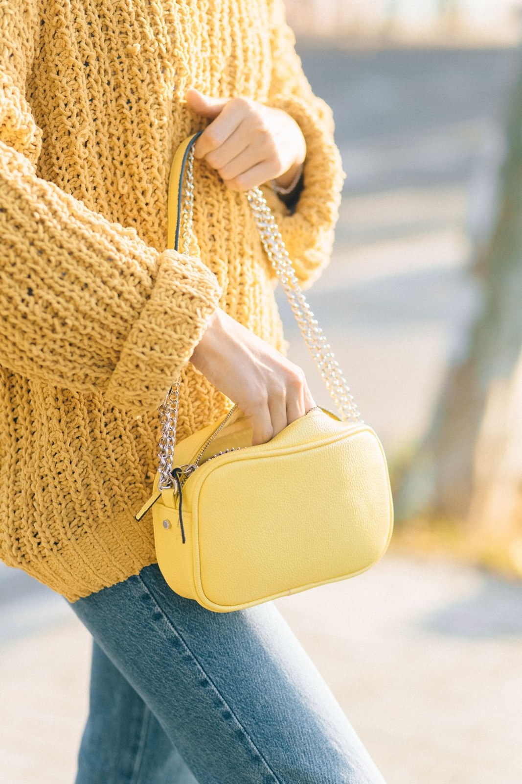 Mustard chunky-knit sweater with blue jeans and a small bright-yellow handbag; detail crop.