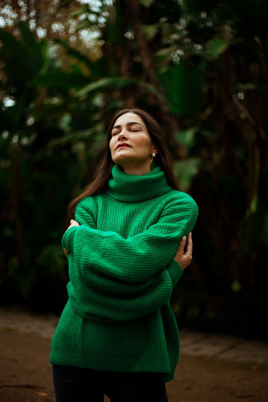 Bright green chunky roll-neck sweater with dark trousers; upper-body outdoor portrait.