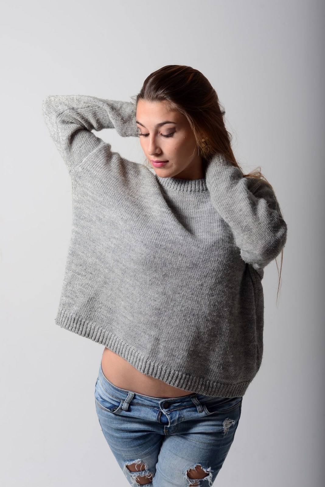 Loose grey knit sweater and ripped blue jeans, cropped above the knees.