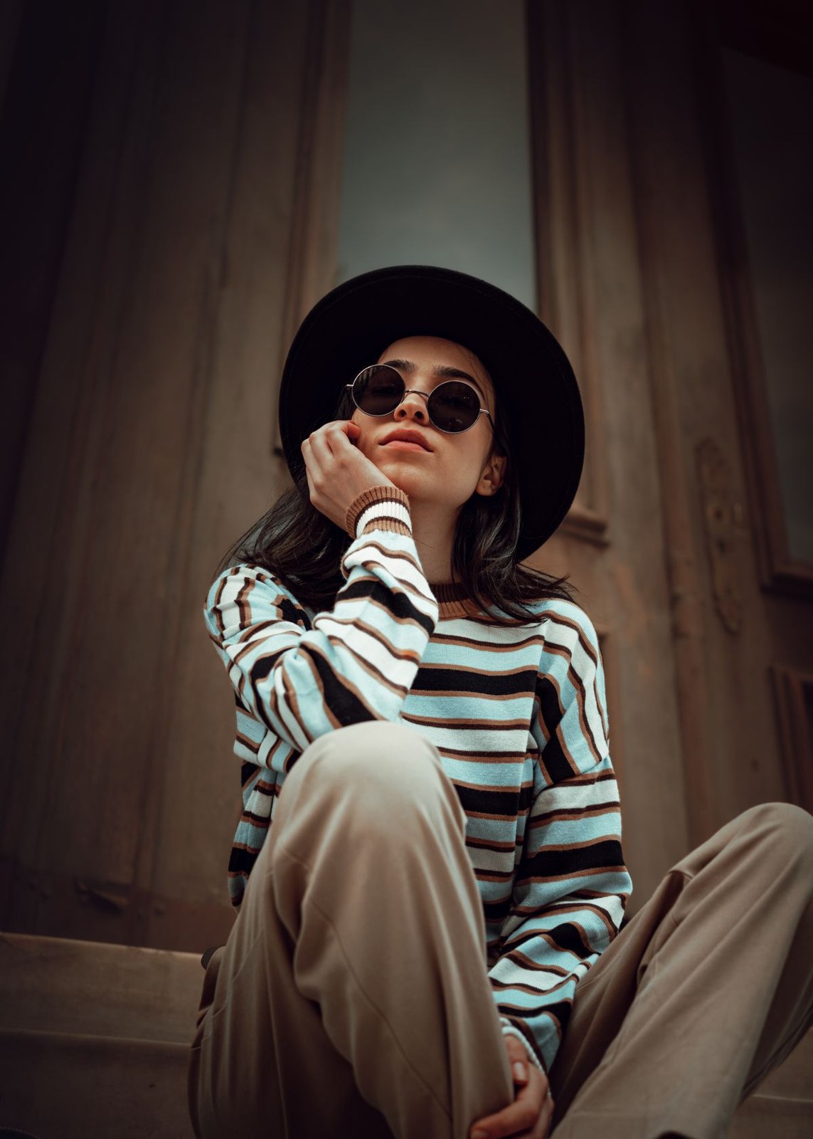 Black-and-white striped long-sleeve top, loose beige trousers, black hat and round sunglasses.