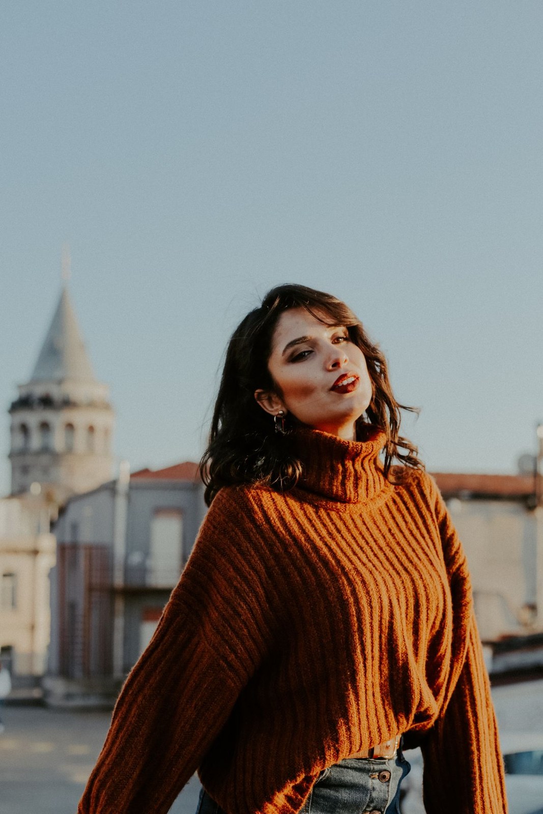 Rust chunky roll-neck sweater with high-waisted dark denim in the city.