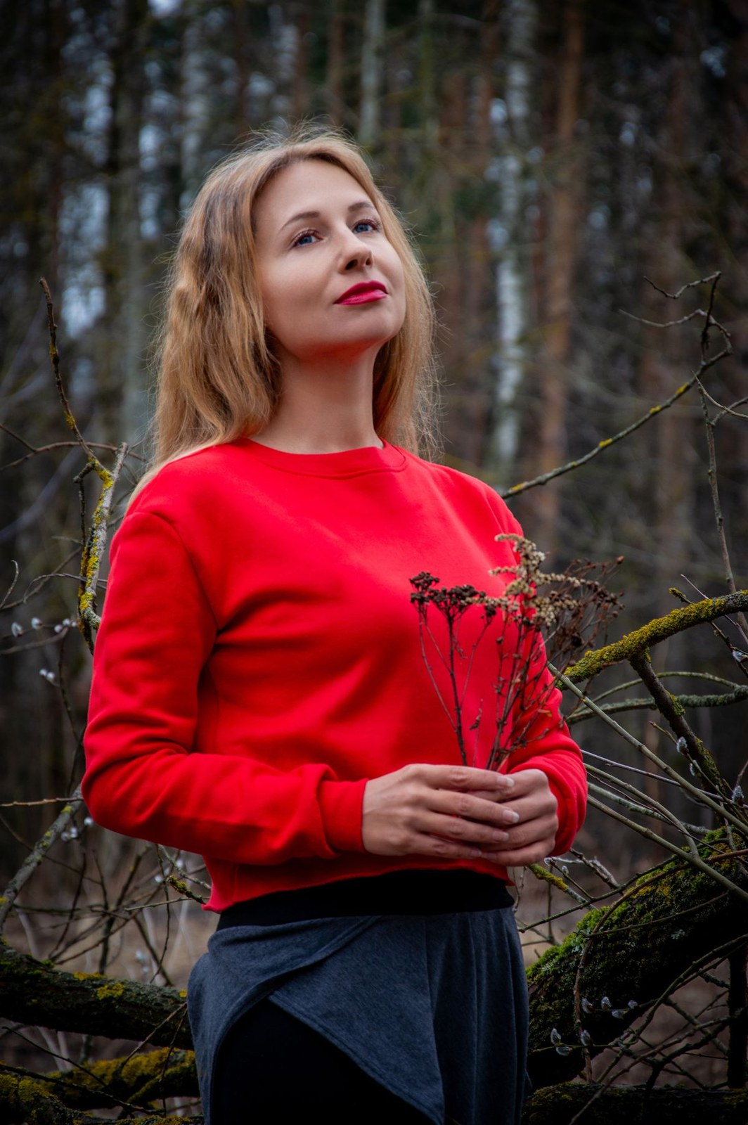 Bright red long-sleeve sweater and dark trousers in a woodland portrait.