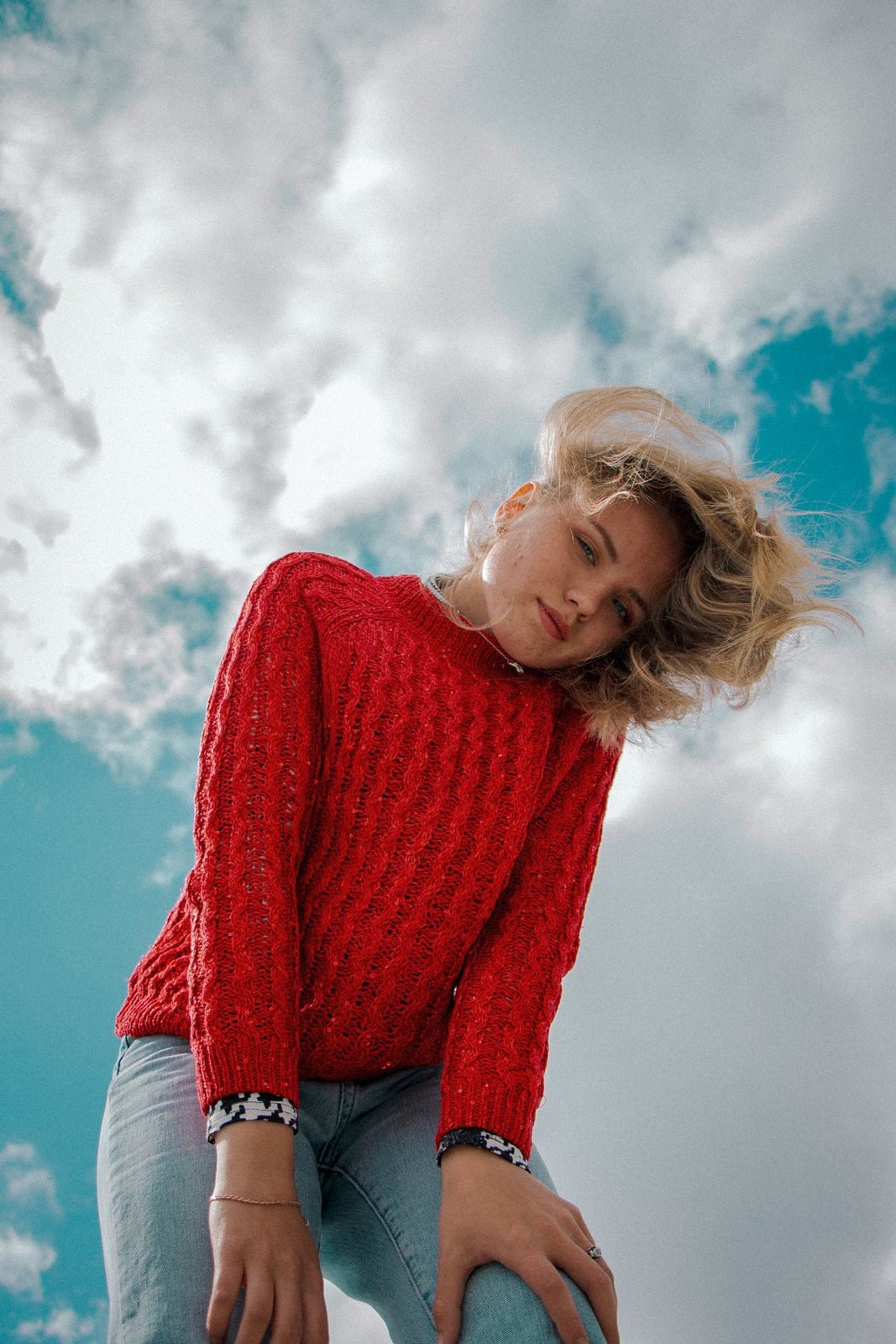 Red textured sweater and pale blue jeans in an outdoor upper-body portrait.