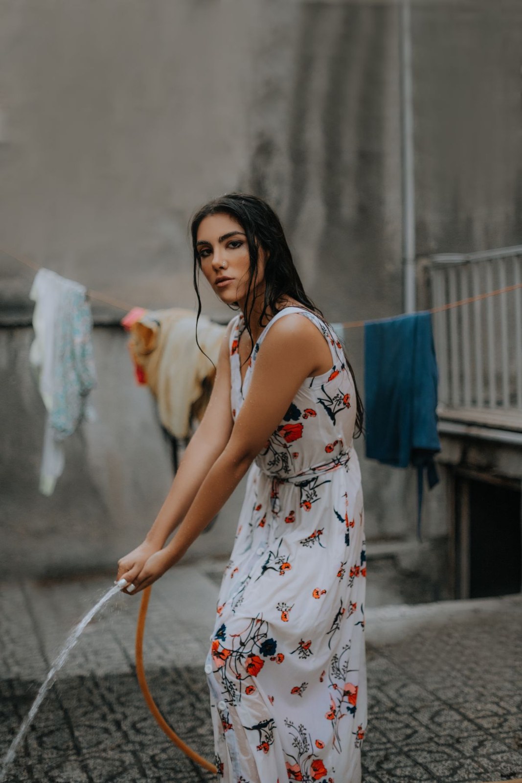 Long white sleeveless floral dress in a courtyard, seen from the side.