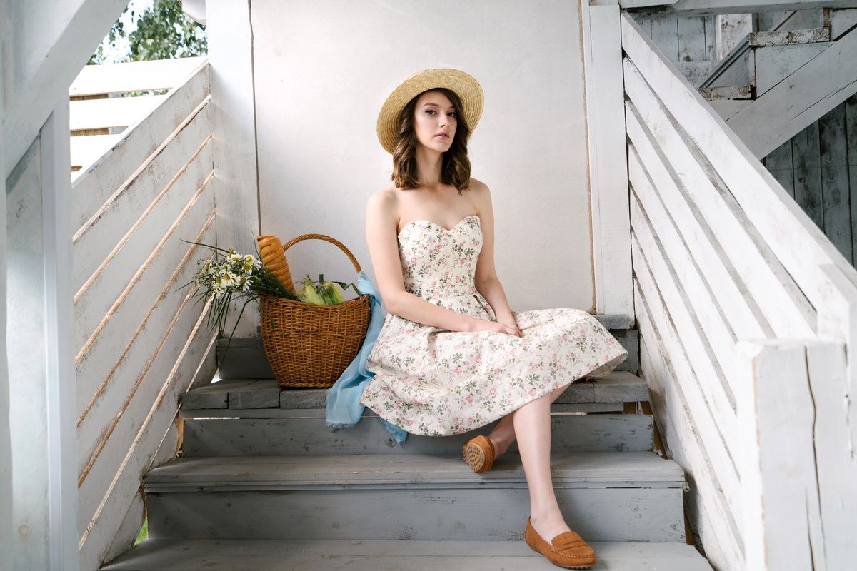 White floral midi dress, pale straw-style hat, basket bag and tan flats on steps.