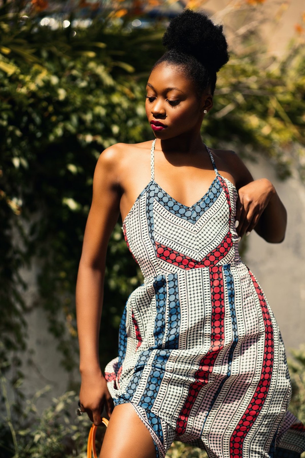 Sleeveless striped and checked dress with thin straps in blue, red and neutral tones outdoors.