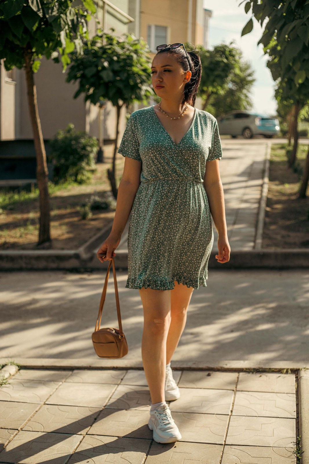 Green small-print short wrap-style dress, white trainers and a small round tan bag.