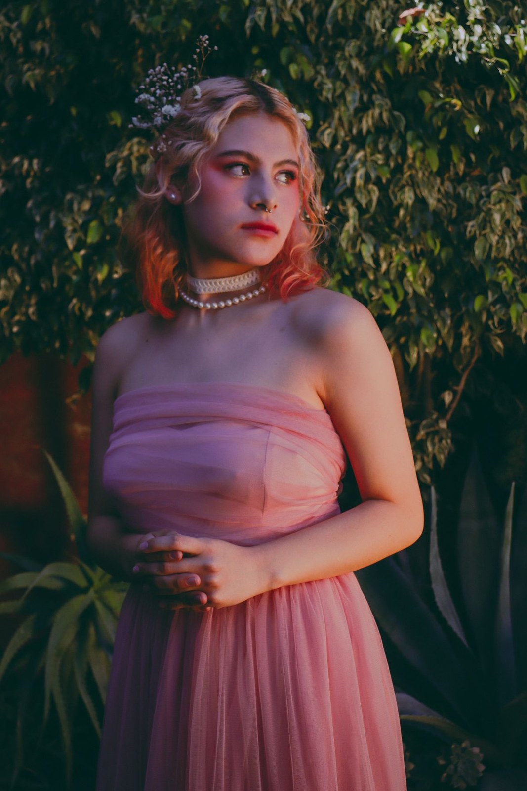 Pink strapless pleated dress and layered pearl necklaces in a garden portrait.