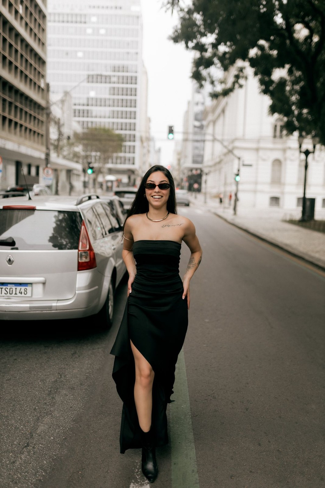Black strapless long dress with a thigh slit, black pointed ankle boots and sunglasses on a city street.