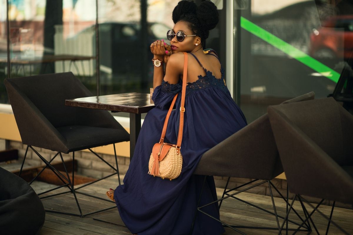 Loose navy sleeveless long dress, round tan shoulder bag and sunglasses at an outdoor café.