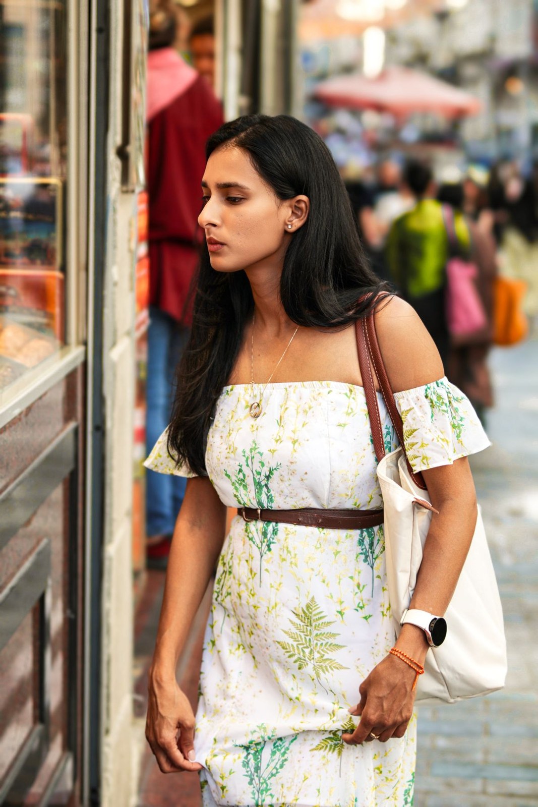 White botanical-print off-shoulder dress with a narrow dark belt and pale shoulder bag.