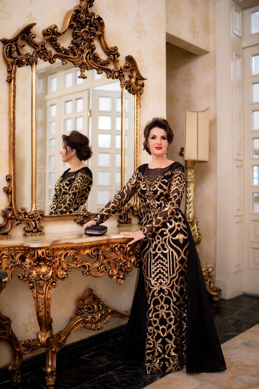Long black gown with ornate gold pattern and long decorative sleeves beside a mirror.