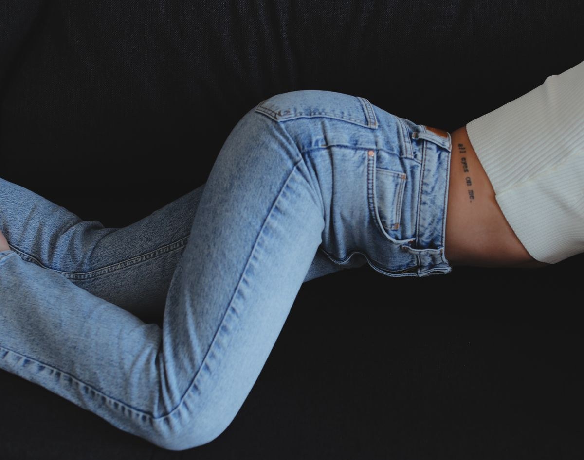 Detail of light-blue slim jeans with a pale cropped knit top against a dark background.