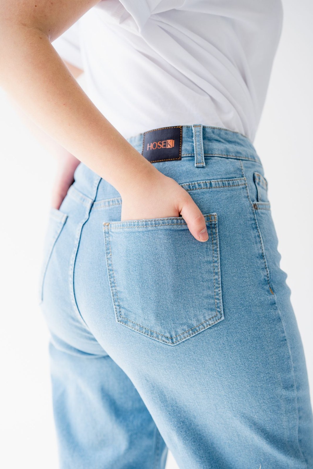 Back-pocket detail of light-blue jeans worn with a tucked white top.