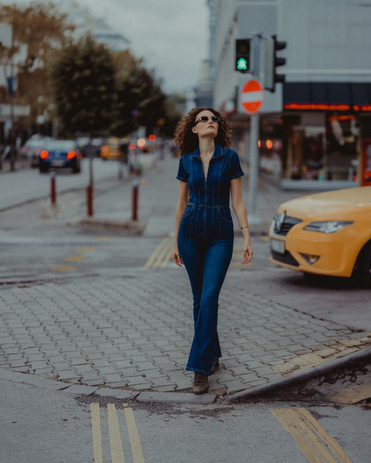 Dark-blue short-sleeve denim-style jumpsuit with flared legs and tan heels on a street.