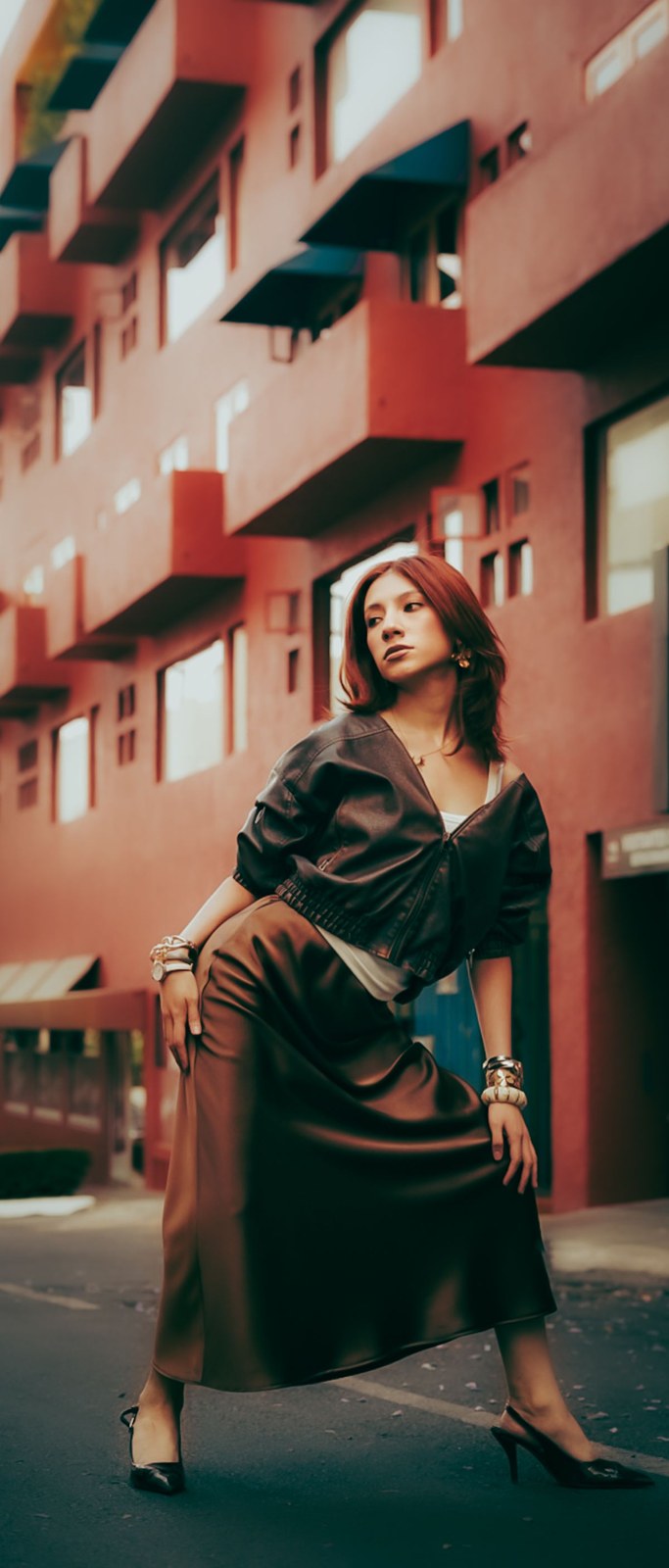 Dark wrap-style top, long brown draped skirt and dark pointed heels by a colourful building.