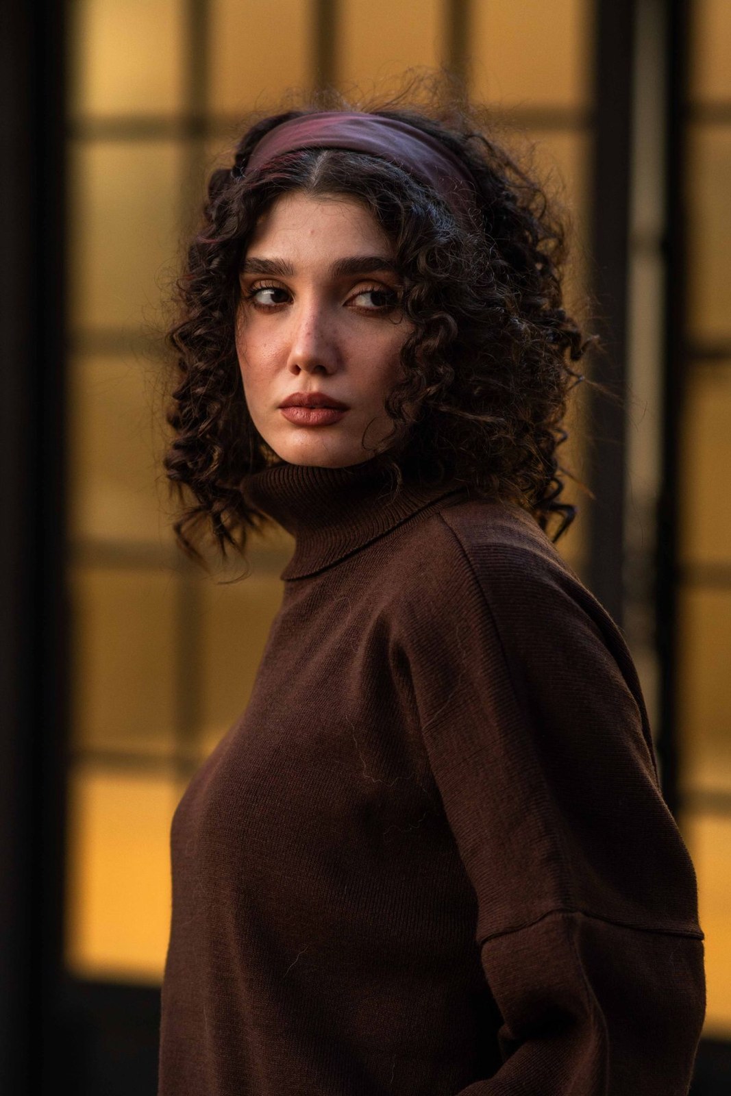 Dark-brown roll-neck sweater and burgundy headband in a close upper-body portrait.