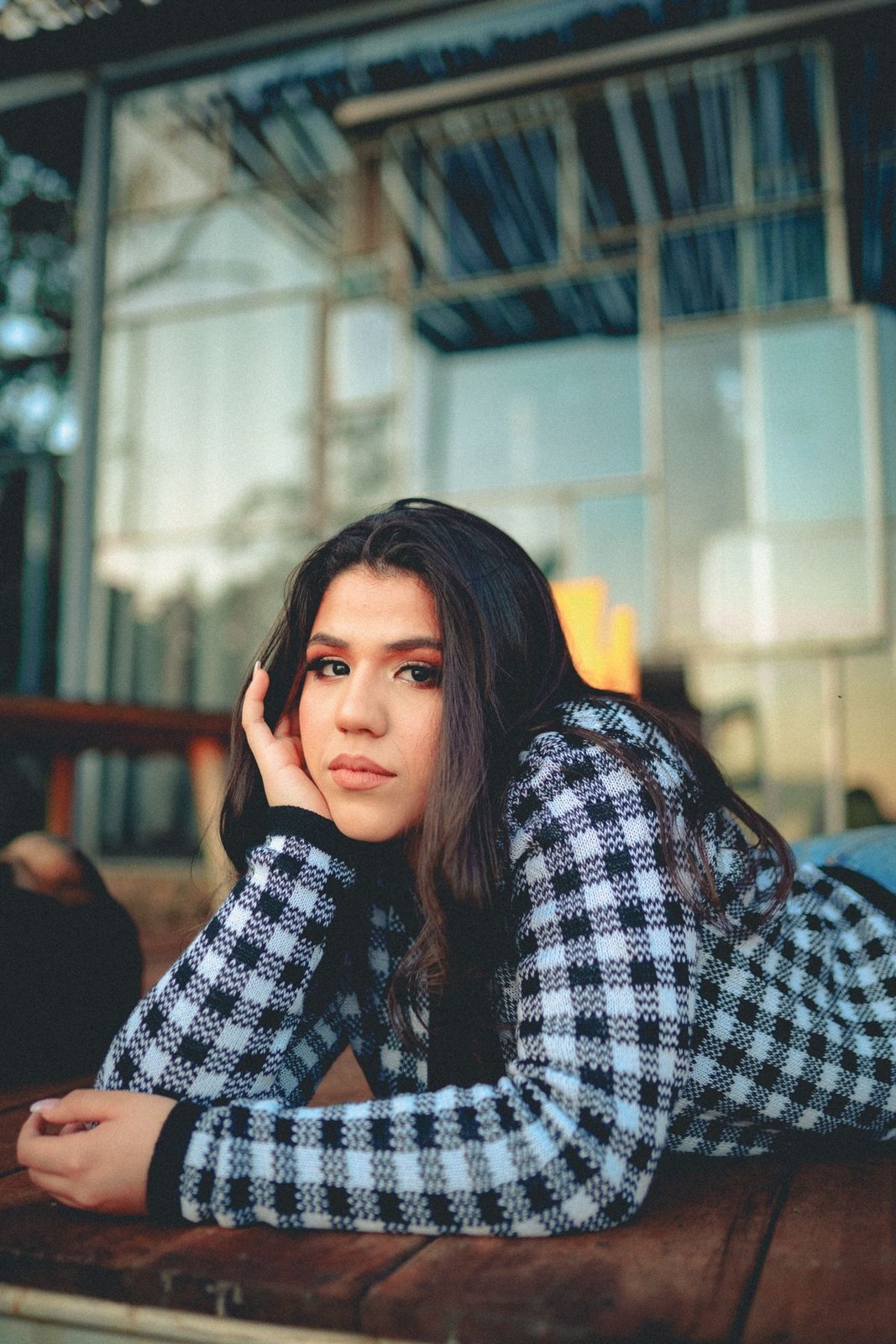 Black-and-white checked long-sleeve top and pale jeans, leaning across a café table.