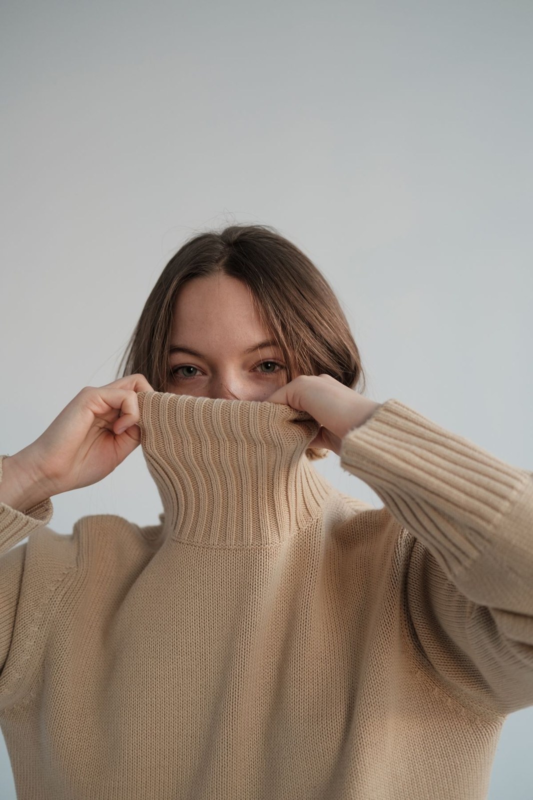 Beige wide-rib roll-neck sweater in a close portrait, collar pulled up near the face.
