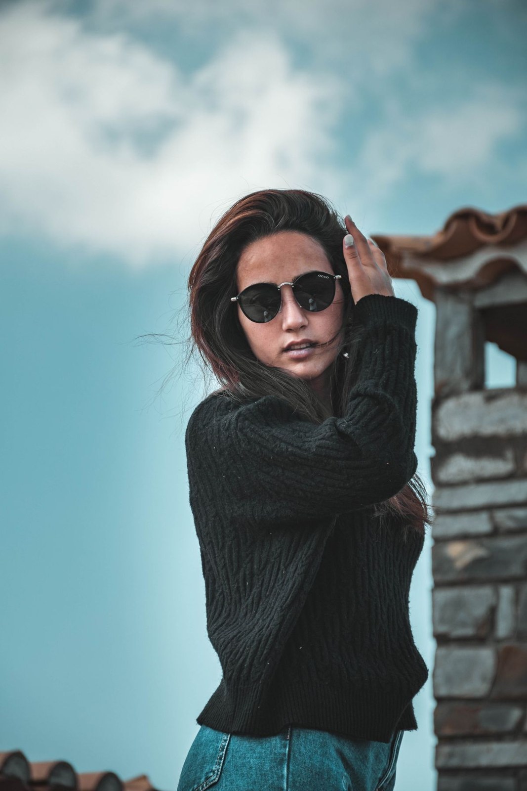 Black ribbed roll-neck sweater, blue jeans and round sunglasses in an upper-body outdoor crop.