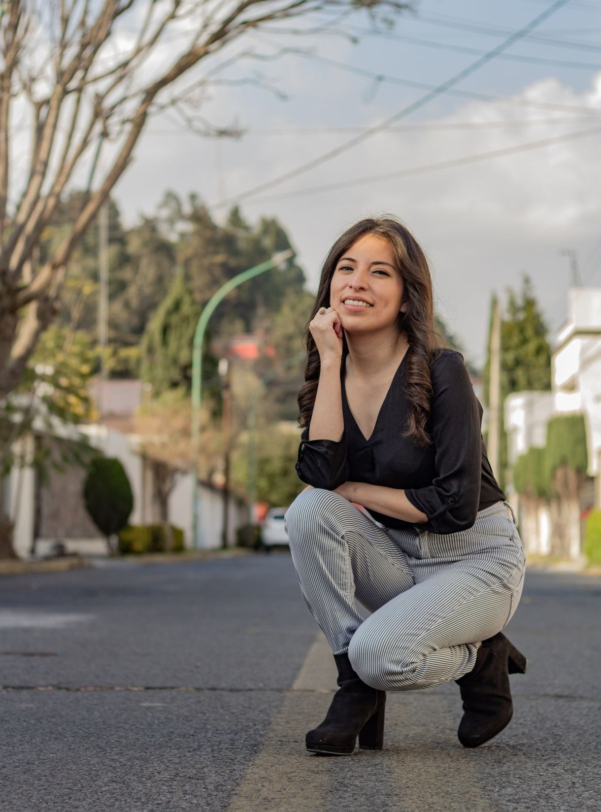 Black crossover blouse, light-grey jeans and black ankle boots in a crouching street pose.